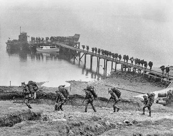 Soldiers of 5 Infantry Brigade disembark at a jetty from one of HMS INTREPID's landing craft at San Carlos Water in the Falkland Islands 1 June 1982